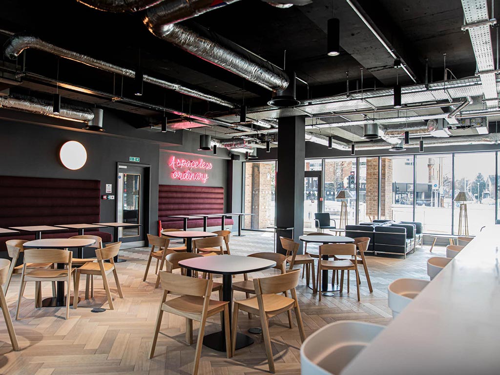 Interior view of a modern cafe or lounge area, with tables, chairs, and an exposed ceiling